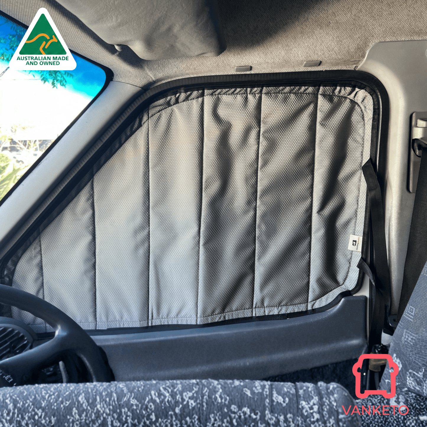 A gray car window shade installed on the driver's side window of a vehicle, shown with the steering wheel and interior cabin visible. A logo for 'Australian Made and Vanned' appears in the top-left corner, and a 'VAVNETS' logo is in the bottom-right corner.