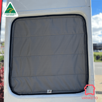 A gray padded window cover with a black trim installed on a white vehicle window, with outdoor scenery blurred in the background. A Vanketo logo is visible in the bottom right corner.