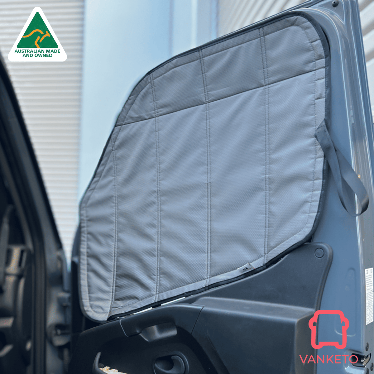 A gray padded car window shade installed on the open door of a vehicle, shown in a real outdoor setting with a building facade in the background. A Vanketo logo appears in the bottom right corner, and an Australian Made and Vefined badge appears in the top left.