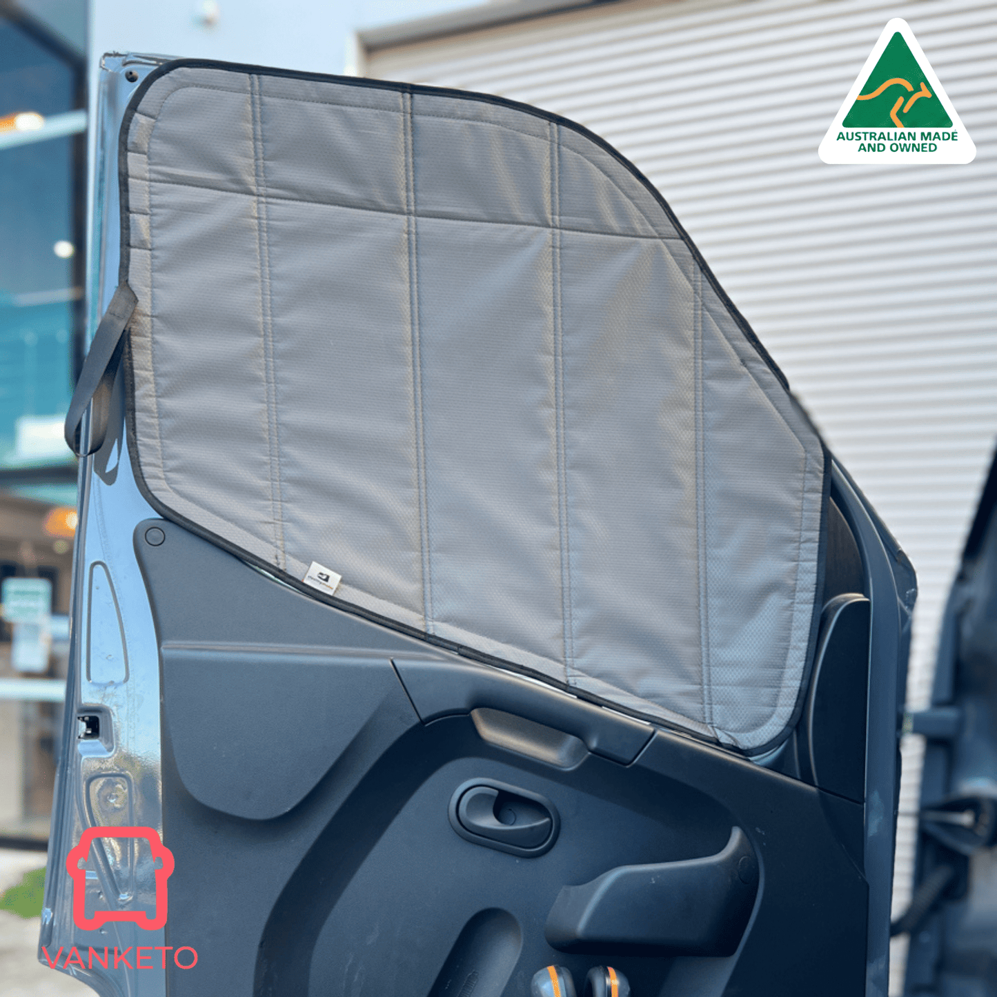 A gray padded car door sun shade installed on the inside of a vehicle door, shown outdoors with a corrugated metal building in the background. A small 'VANNETO' brand logo is visible on the shade, and an 'Australian Made' badge appears in the top right corner.