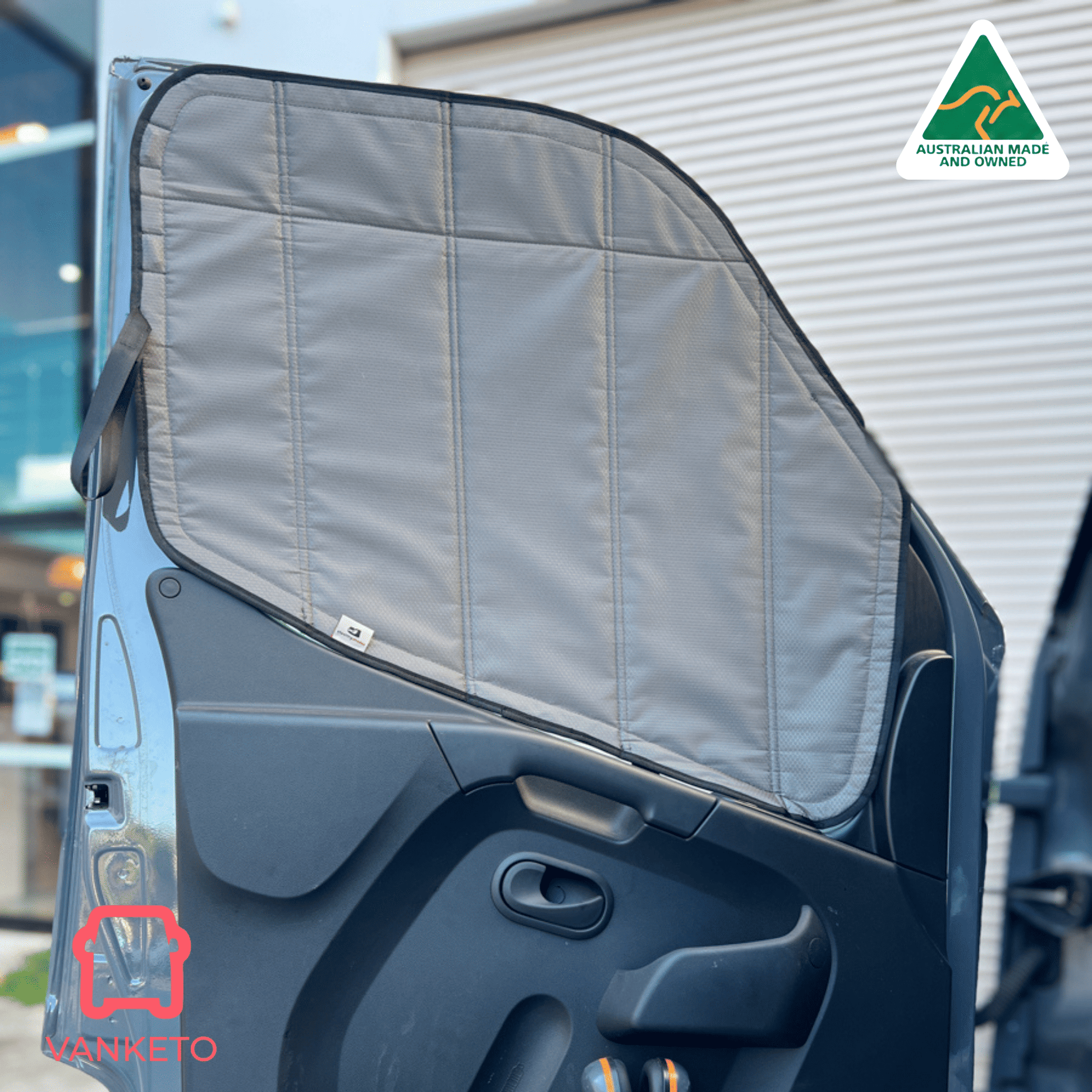 A gray padded car door sun shade installed on the inside of a vehicle door, shown outdoors with a corrugated metal building in the background. A small 'VANNETO' brand logo is visible on the shade, and an 'Australian Made' badge appears in the top right corner.